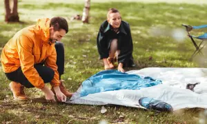 Mann und Frau bereiten ihr Zelt vor. Sie legen die Zeltplane aus, um das Zelt zu reinigen und aufzubauen.
