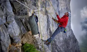 Bergsteiger sichert den nachstieg an der Felswand. Seile, Rucksack und Ausrüstung sind sichtbar.