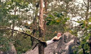 Frau ruht sich nach dem Fontainebleau Bouldern auf einem Felsen aus, umgeben von Bäumen.