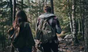 Zwei Personen mit Rucksäcken wandern durch einen Wald. Ein Mann und eine Frau, die sich auf ein Abenteuer vorbereiten, das über einfaches Hiking hinausgeht und eher dem Trekking ähnelt.
