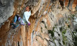 Eine Frau klettert eine steile Felswand hoch. Sie konzentriert sich auf den nächsten Griff, während sie sich beim **rotpunkt klettern** anstrengt.