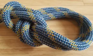 Eine detaillierte bulin knoten anleitung zeigt, wie man diesen sicheren Knoten knüpft. Das Seil ist blau-gelb gemustert.
