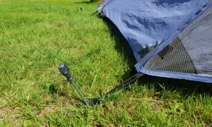 Ein Zelt wird mit Heringen im Gras abgespannt. Ein Hering ragt aus dem Boden, um das Zelt zu sichern.