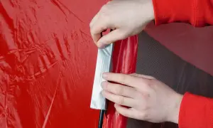 Hände reparieren mit Klebeband eine rote Zeltplane.