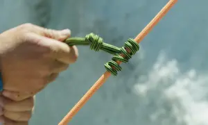 Eine Hand bindet einen HMS Knoten auf ein oranges Seil.