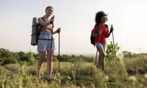 Zwei Frauen genießen eine 10 km Wanderung gesund in der Natur. Sie tragen Rucksäcke und Trekkingstöcke.