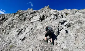 Frau klettert einen steilen Felsgrat im 3. Grad. Der Himmel ist strahlend blau.