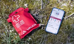 Rote Erste-Hilfe-Tasche und Smartphone mit Notruf-App liegen im Gras. Wichtige erste hilfe basics für unterwegs.