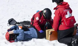 Bergretter kümmern sich nach einem Sturz auf Knie um einen verletzten Skifahrer im Schnee.
