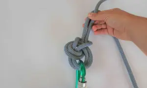 Hand hält ein Seil, das zu einem dicken Knoten gebunden ist, der an einem Karabiner befestigt ist.