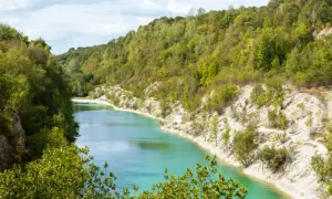 Ein malerischer Weg lädt zum **wandern am Wasser** ein. Türkisblaue Fluten schlängeln sich durch eine grüne Hügellandschaft mit steilen, weißen Ufern.