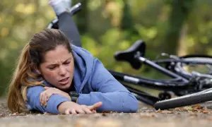 Junge Frau nach einem Sturz auf den Brustkorb, Fahrrad liegt daneben. Sie hält sich den Arm und hat Schmerzen.