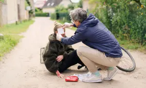Erste Hilfe nach einem Sturz: Ein Mann versorgt eine Frau mit aufgeschürfter Hand und einem Verband am Auge.