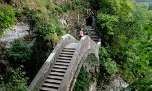Eine Frau genießt die Aussicht auf einer Steinbrücke, während sie in Inzigkofen wandert. Treppen führen zu einer Höhle.
