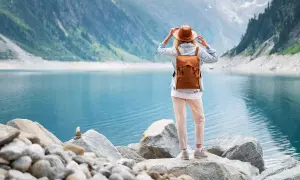 Frau mit Rucksack und Hut steht am Ufer eines türkisfarbenen Sees in den Bergen. Ein malerischer Ausblick, wie man ihn in Seen Deutschland findet.