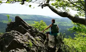 Frau mit Rucksack auf Felsen, genießt Aussicht auf bewaldete Hügel. Perfekt für eine 3 Tage Wanderung Deutschland.