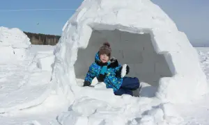 Kind im selbstgebauten Iglu, bereit für Winterabenteuer.