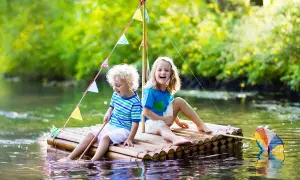 Zwei Kinder bauen einen Floss und genießen den Sommer auf dem Wasser.