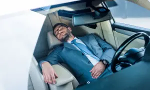 Mann im Anzug schläft im Auto. Ob man in Italien im Auto schlafen darf, ist eine andere Frage.