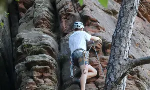 Ein Kletterer meistert eine Route im 2. Grad an einer roten Felswand, gesichert durch ein Seil.