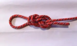 Ein rotes Seil mit schwarzen und weißen Mustern bildet einen Achterknoten, der sicher und stabil aussieht.