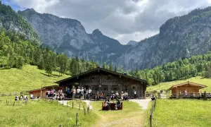 Eine Berghütte mit Gästen vor einer beeindruckenden Bergkulisse, die an ein steinernes Meer erinnert.