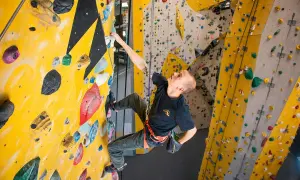 Mann klettert an einer gelben Wand mit bunten Griffen. Verschiedene klettern arten sind hier möglich.
