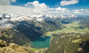 Blick ins Tannheimer Tal mit türkisfarbenem See, grünen Wäldern und schneebedeckten Gipfeln. Entdecken Sie hier Tannheimer Tal Geheimtipps!