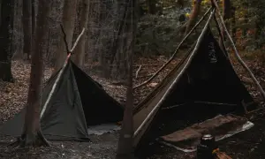 Zelt aufbauen Anleitung: Ein Tipi-Zelt aus Stoff, gestützt von Ästen, im Wald. Innen liegen Decken und eine Teekanne.