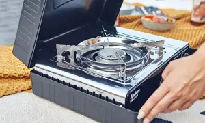 Ein Campingkocher mit offenem Deckel, bereit für die Zubereitung von Speisen. Die richtige Lagerung von Gaskartuschen ist wichtig für die Sicherheit.