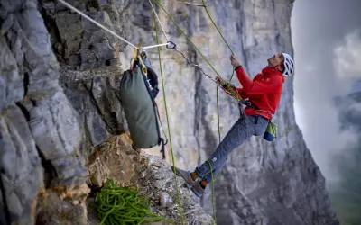 Bergsteiger sichert den nachstieg an der Felswand. Seile, Rucksack und Ausrüstung sind sichtbar.