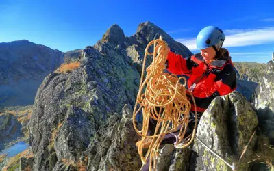 Bergsteigerin mit Seil in den Bergen, bereitet sich auf das Klettern vor und achtet auf wichtige Knoten.