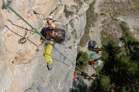 Frau klettert an einer Felswand bei Briançon, während unten ein Team wartet.