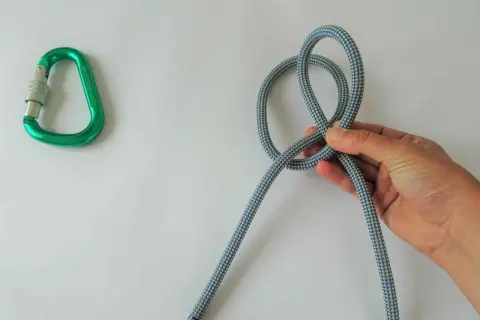 Hand knotet Seil, ein Karabiner liegt daneben. Dies ist der beste Knoten für Sicherheit.