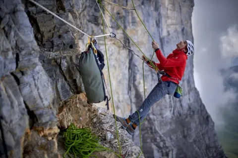 Bergsteiger sichert den nachstieg an der Felswand. Seile, Rucksack und Ausrüstung sind sichtbar.