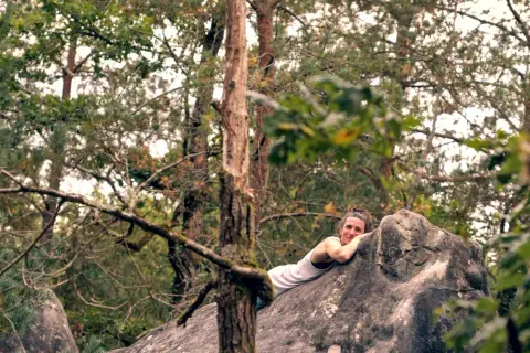 Frau ruht sich nach dem Fontainebleau Bouldern auf einem Felsen aus, umgeben von Bäumen.