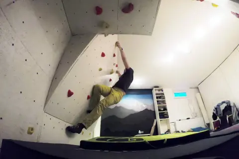 Mann klettert an einer selbstgebauten Boulderwand. Bunte Griffe sind auf der Wand verteilt.