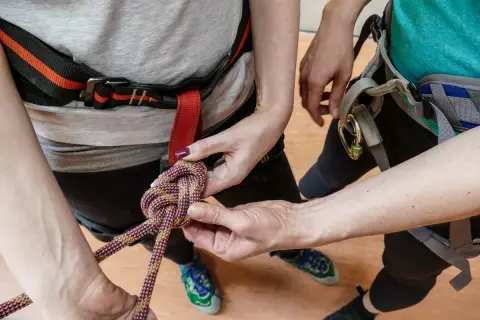 Hände knüpfen einen Achterknoten an einem Klettergurt. Die Seile sind farbig und der Knoten wird sorgfältig geformt.