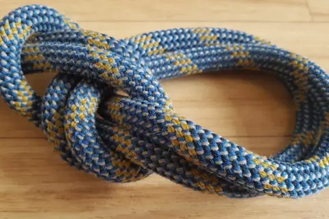 Eine detaillierte bulin knoten anleitung zeigt, wie man diesen sicheren Knoten knüpft. Das Seil ist blau-gelb gemustert.