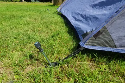 Ein Zelt wird mit Heringen im Gras abgespannt. Ein Hering ragt aus dem Boden, um das Zelt zu sichern.