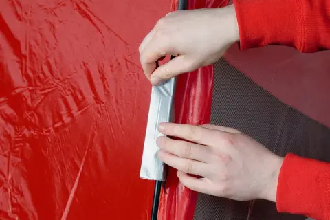 Hände reparieren mit Klebeband eine rote Zeltplane.