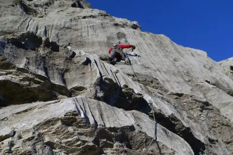Marcel Dettling klettert eine steile Felswand empor, gesichert durch ein Seil. Der blaue Himmel bildet einen starken Kontrast zum grauen Gestein.