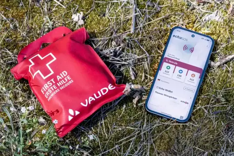 Rote Erste-Hilfe-Tasche und Smartphone mit Notruf-App liegen im Gras. Wichtige erste hilfe basics für unterwegs.