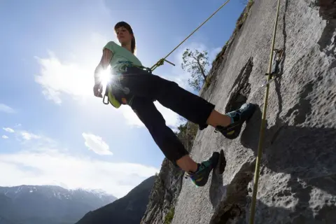 Eine Kletterin seilt sich ab. Das Abseilen bedeutet hier, sicher den Berg hinunterzukommen.