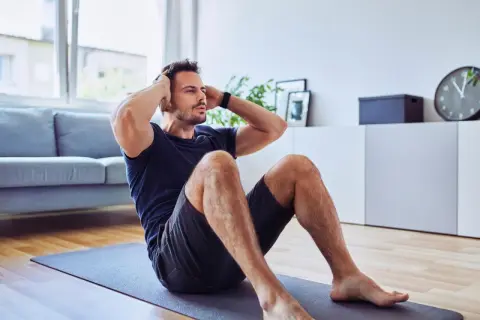 Mann macht Sit-ups auf einer Matte. Er trainiert trotz eines möglichen Rippenbruchs, um fit zu bleiben.