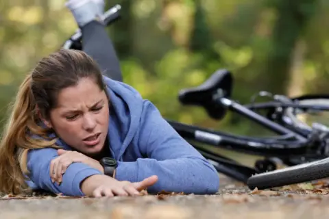 Junge Frau nach einem Sturz auf den Brustkorb, Fahrrad liegt daneben. Sie hält sich den Arm und hat Schmerzen.