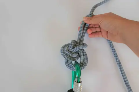 Hand tying a figure-eight knot, a **guter knoten** for climbing, through a carabiner.