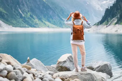 Frau mit Rucksack und Hut steht am Ufer eines türkisfarbenen Sees in den Bergen. Ein malerischer Ausblick, wie man ihn in Seen Deutschland findet.