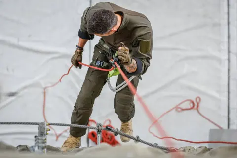 Mann in Uniform übt das Abseilen nur mit Seil. Er hält das Seil fest und kontrolliert den Abstieg.