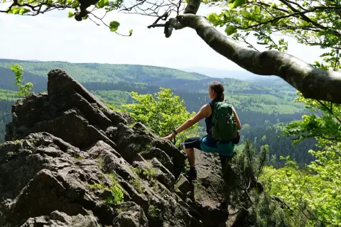 Frau mit Rucksack auf Felsen, genießt Aussicht auf bewaldete Hügel. Perfekt für eine 3 Tage Wanderung Deutschland.